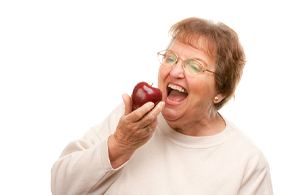 Woman with an implant-retained denture biting an apple.