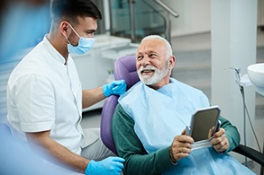 Senior patient looking at dentist while holding small mirror