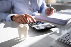 Man at desk with model tooth and binder of paperwork pressing calculator with finger