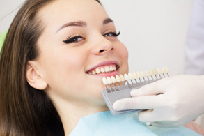 Woman in dental chair smiling with shade guide held to teeth