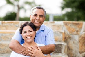 An older couple smiling and hugging outside.