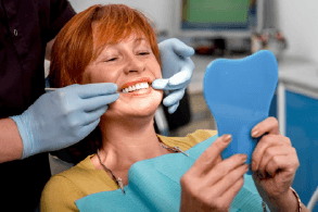 An older woman examining her teeth at the dental office.