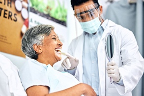 Patient smiling at reflection while dentist holds mirror