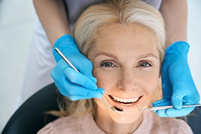 Patient smiling while dentist uses tools to examine teeth