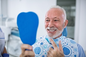 Smiling man looking at reflection in handheld mirror