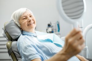 older woman admiring her smile with implant-retained dentures in the mirror