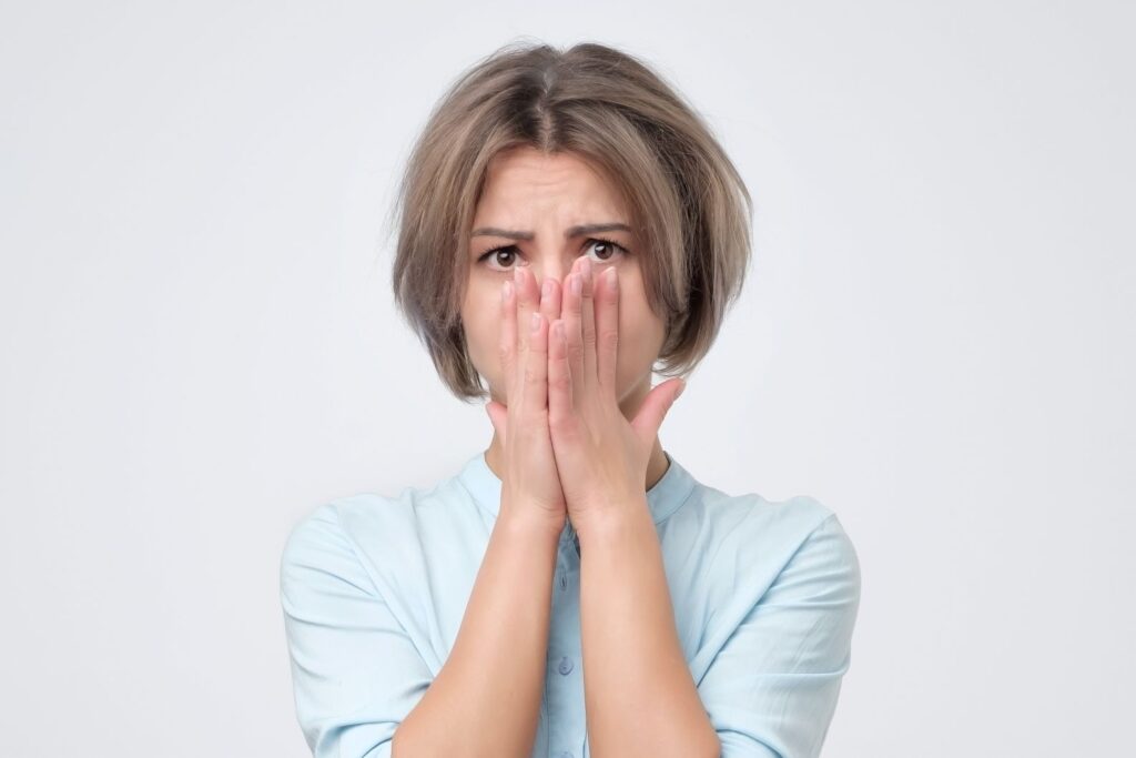 Woman with concerned expression with both hands over her mouth